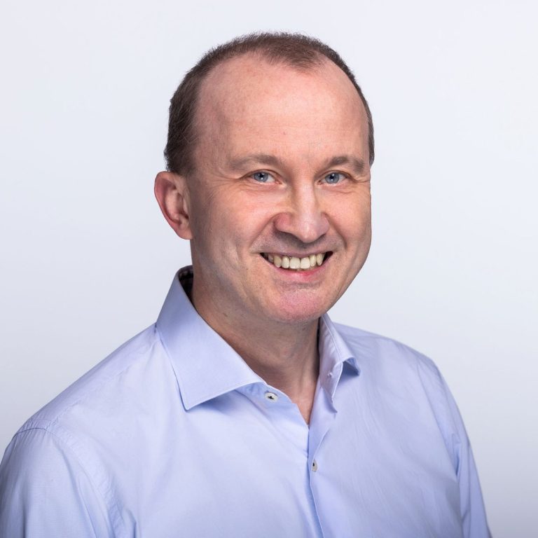 Hartmut Reiners in einem hellblauen Hemd vor hellem Hintergrund.